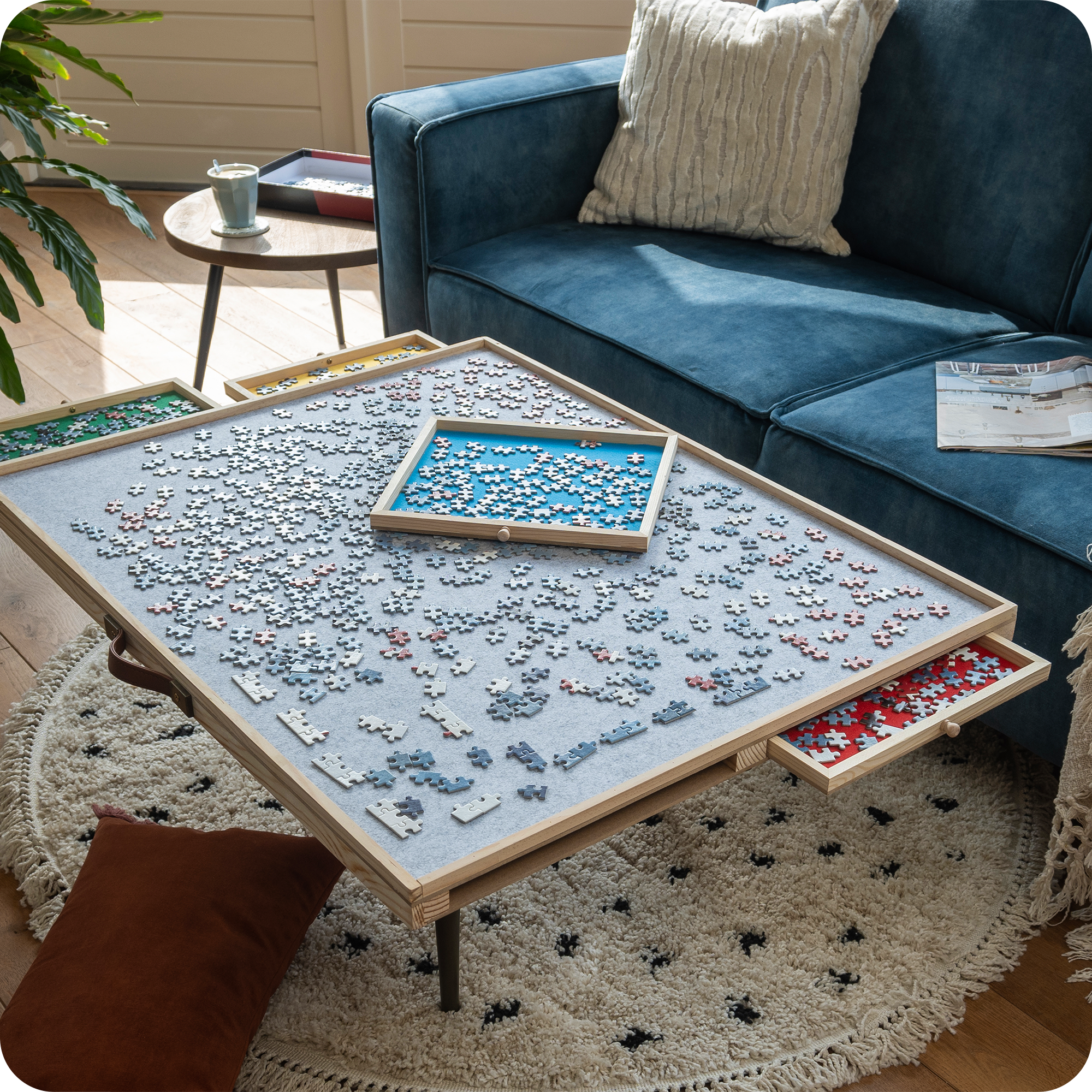 Een moderne woonkamer met een blauwe bank en beige kussens. De verstelbare puzzelplaat staat op de salontafel en er wordt een puzzel van 1500 stukjes op gemaakt.